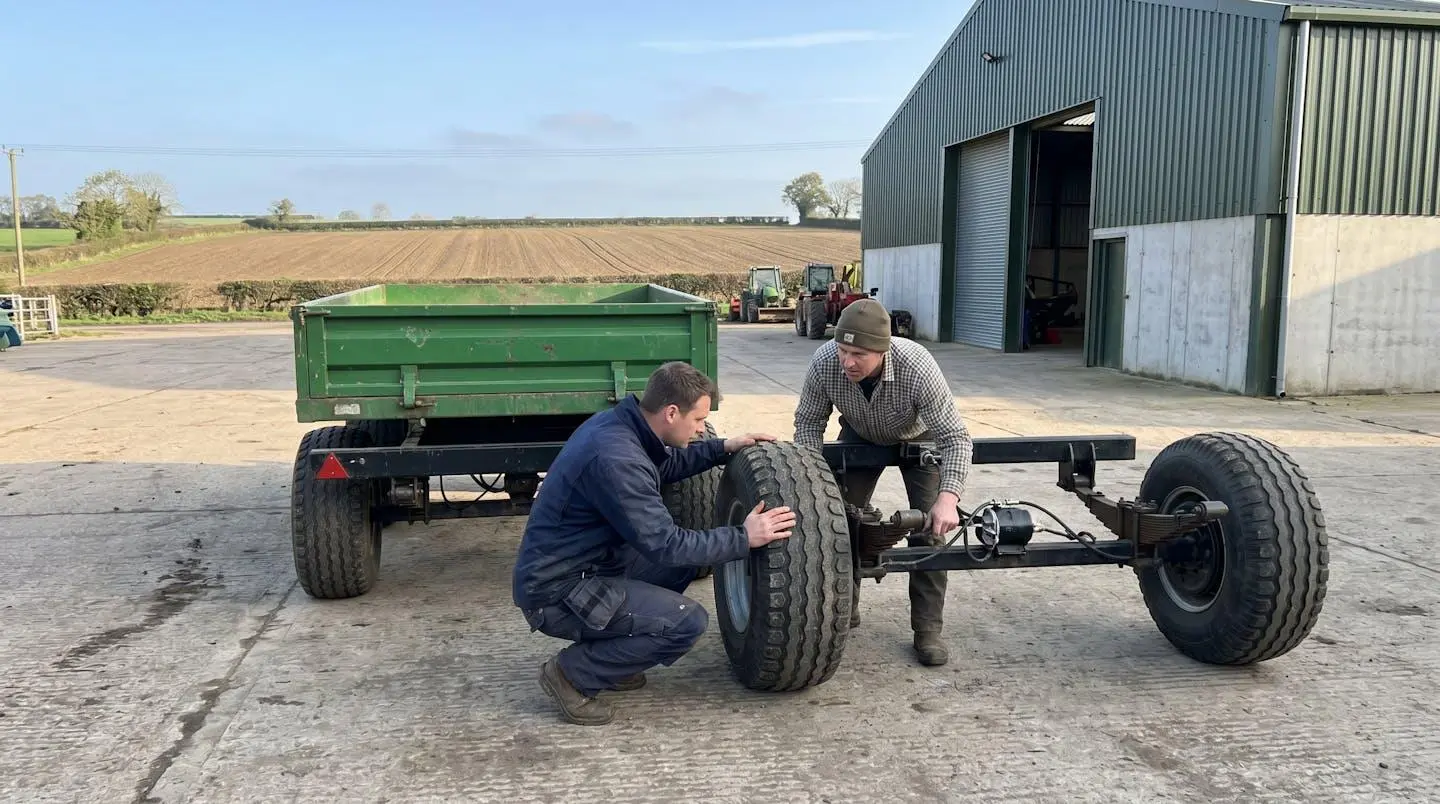 Deux hommes inspectent une remorque agricole d'occasion dans une cour de ferme ensoleillée